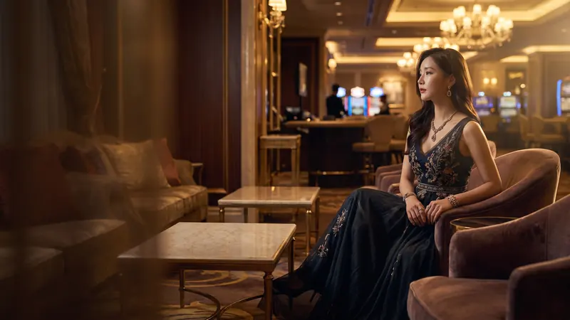 컬러 블록 카지노 배경에서 VIP 라운지 의자에 앉은 이브닝드레스 차림의 여성 – 레고카지노 사칭을 잡아라